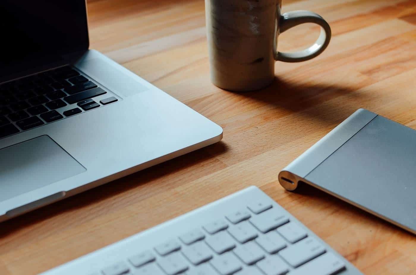 A laptop, keyboard and coffee mug on a timber desk