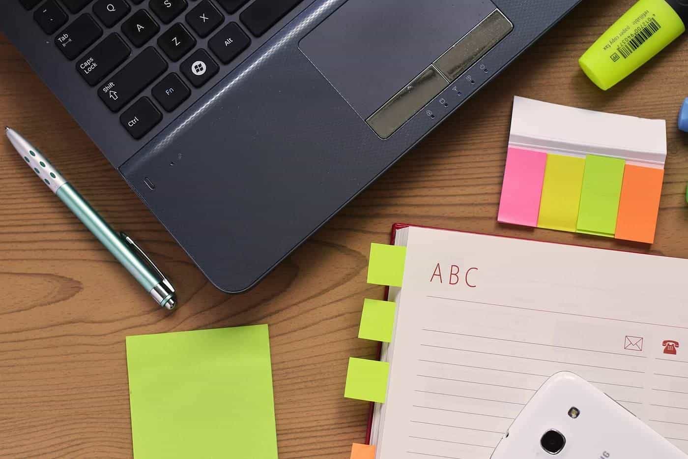 A laptop, notebook, pen and sticky notes on a desk