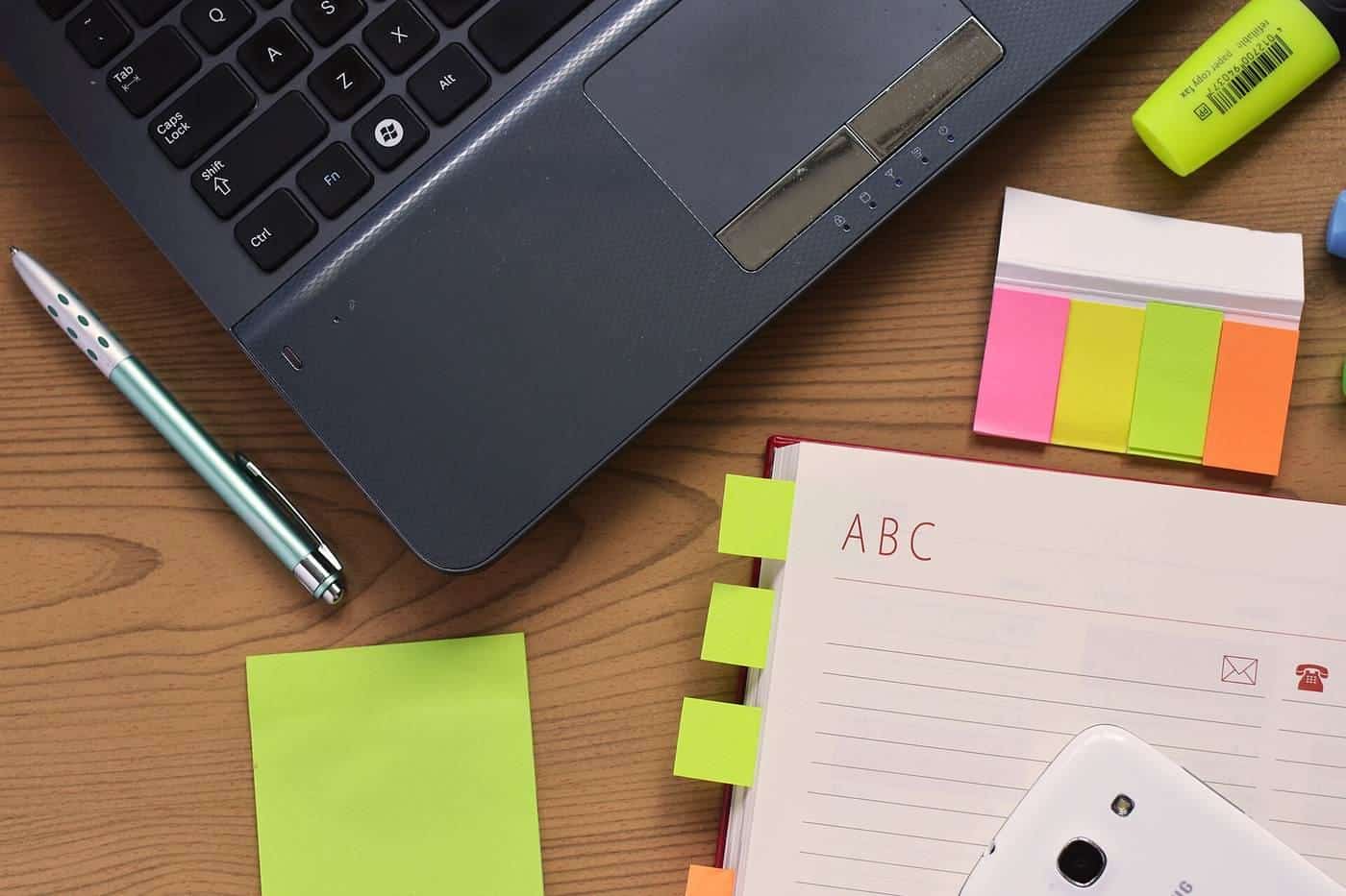 A laptop, notebook, pen and sticky notes on a desk