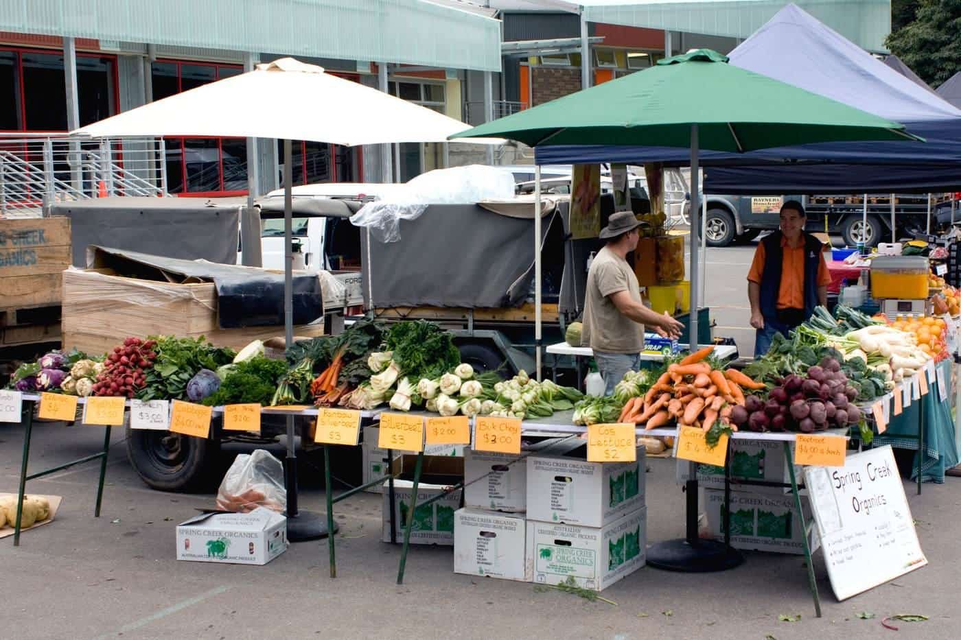 A fruit and vegetable stall with customers at an outdoor farmers market